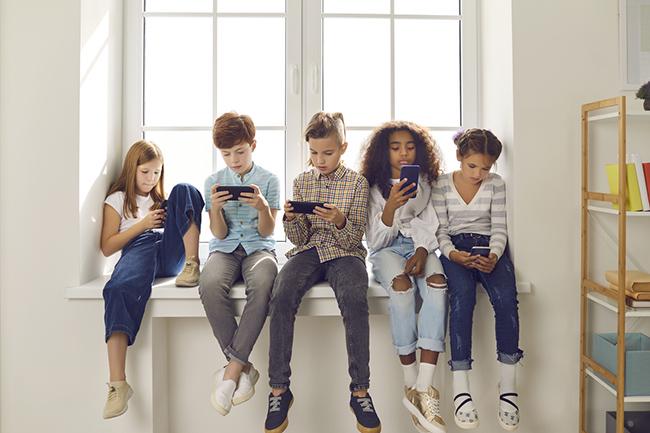 Five children sat on a windowsill looking at their mobile phones